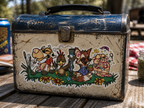THC Farm sticker placed on scratched vintage metal lunchbox at outdoor picnic table