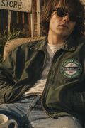 THC Humboldt Patch displayed on the chest of an olive canvas jacket worn by a laid-back musician relaxing outside a rustic cabin, featuring a vintage California Grown embroidered design inspired by classic Northern California style