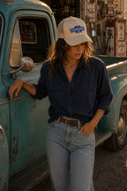 THC Chronic Patch displayed on the front of a cream trucker hat worn by a young woman beside a weathered turquoise vintage pickup truck outside a rustic California desert garage featuring a blue and white embroidered automotive-inspired design