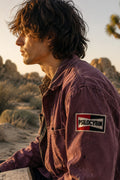 THC Psilocybin Patch displayed on the upper sleeve of a faded plum canvas chore jacket worn by a young artist in Joshua Tree at golden hour, featuring a retro embroidered psilocybin graphic in red, black, and white