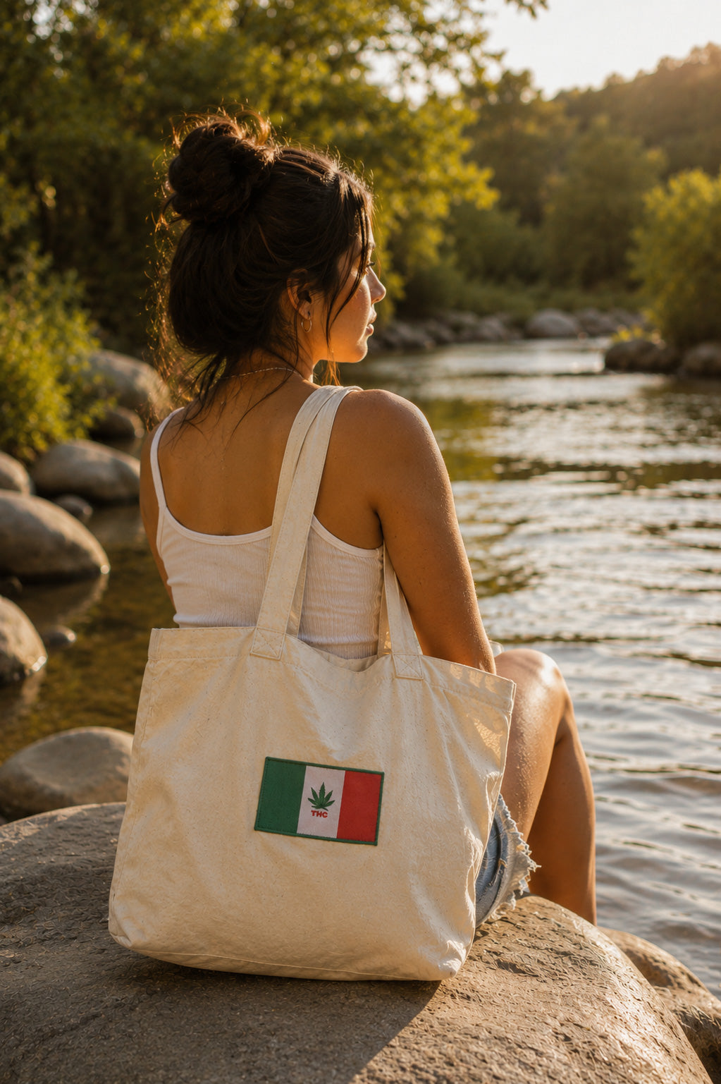 THC Mexico Flag Patch displayed on a natural canvas tote bag beside a young woman sitting on a riverside stone looking over a calm river featuring a green, white, and red embroidered Mexico-inspired flag with a cannabis leaf centerpiece