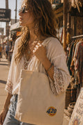 THC 420 Sun Patch displayed on a natural canvas tote bag carried by a young bohemian woman on the Venice Beach boardwalk, featuring a retro embroidered 420 sun design in yellow, orange, blue, and white