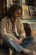 THC Microdot Patch displayed on the right knee of heavily faded blue jeans worn by a laid-back indie musician sitting outside a neighborhood record shop featuring the Window to the Mind embroidered graphic