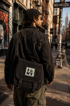 THC Leaf NY Patch displayed on the front flap of a black canvas messenger bag carried through the streets of New York City, featuring an embroidered cannabis leaf in a classic New York-inspired design