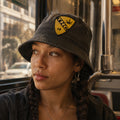 THC Air Cav Patch displayed on a faded black bucket hat worn by a young woman riding public transit in San Francisco featuring a yellow and black embroidered aviation-inspired shield with a cannabis leaf graphic