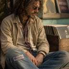 THC Microdot Patch displayed on the right knee of heavily faded blue jeans worn by a laid-back indie musician sitting outside a neighborhood record shop featuring the Window to the Mind embroidered graphic