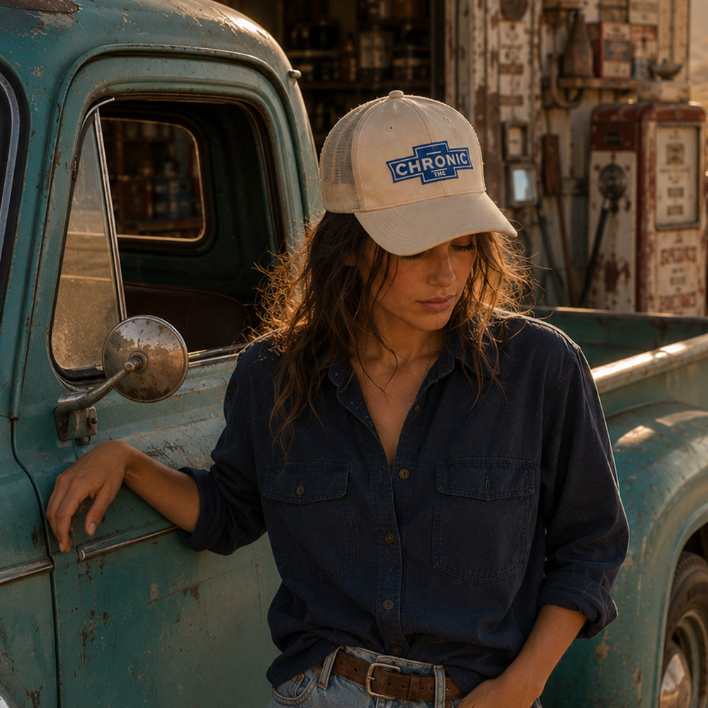 THC Chronic Patch displayed on the front of a cream trucker hat worn by a young woman beside a weathered turquoise vintage pickup truck outside a rustic California desert garage featuring a blue and white embroidered automotive-inspired design