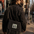 THC Leaf NY Patch displayed on the front flap of a black canvas messenger bag carried through the streets of New York City, featuring an embroidered cannabis leaf in a classic New York-inspired design