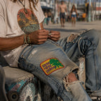 THC See Me Patch displayed on the thigh of distressed denim jeans worn at Venice Beach, featuring retro embroidered lettering with vibrant cannabis leaf artwork