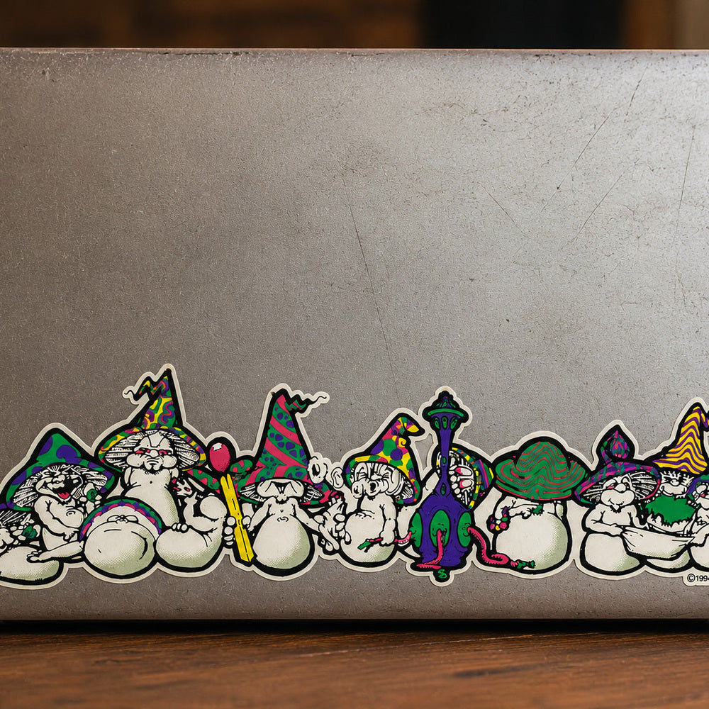 THC Mushrooms sticker stretched across bottom edge of worn laptop with scratches and multiple decals