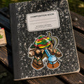 THC Rasta Joe sticker on black composition notebook on worn wooden park bench in outdoor setting