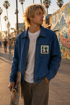 THC Leaf LA Patch displayed on the chest pocket of a blue canvas jacket worn by a young skateboarder on the Venice Beach boardwalk, featuring an embroidered cannabis leaf in a classic Los Angeles-inspired design