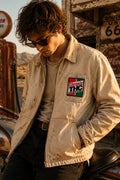 THC Super Kind Patch displayed on the left chest pocket of a faded cream canvas mechanic jacket worn by a young rider at a vintage California desert gas station, featuring a retro embroidered cannabis-inspired design