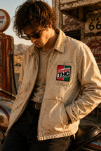 THC Super Kind Patch displayed on the left chest pocket of a faded cream canvas mechanic jacket worn by a young rider at a vintage California desert gas station, featuring a retro embroidered cannabis-inspired design