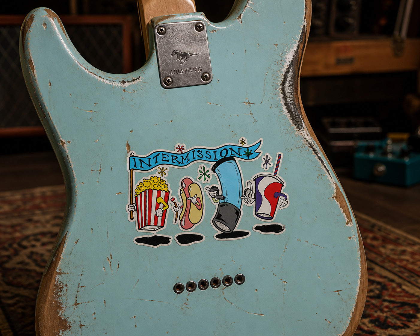 THC Intermission sticker on worn robin’s egg blue Mustang guitar with chipped paint and studio background