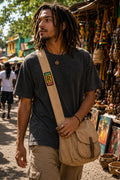 THC Rollin Rasta Patch displayed vertically on the strap of a natural tan canvas crossbody satchel worn by a young musician at an outdoor street market, featuring a reggae-inspired embroidered design